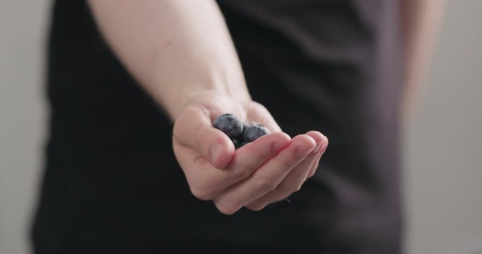 Slow motion man hand show big ripe blueberries on neutral background