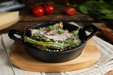 Tasty meat served with asparagus and sprouts in portioned frying pan on table
