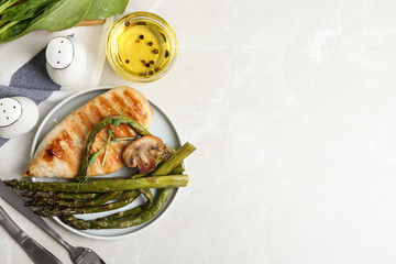 Tasty grilled chicken fillet served with asparagus on light grey marble table, flat lay. Space for text