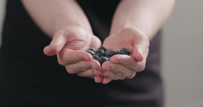 Slow motion man hands show big ripe blueberries on neutral background
