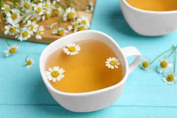 Fresh chamomile tea in cup on light blue wooden table
