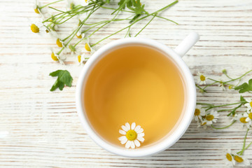 Cup of tea and chamomile flowers on white wooden table, flat lay