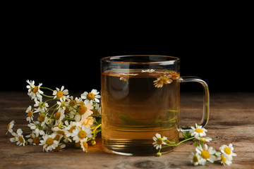 Cup of tea and chamomile flowers on wooden table