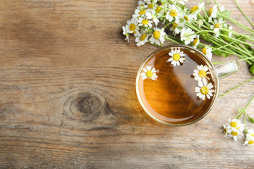 Cup of tea and chamomile flowers on wooden table, flat lay. Space for text