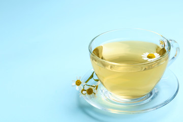 Delicious chamomile tea in glass cup on light blue background. Space for text