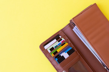 Brown wallet full of credit and discount cards and american dollar banknotes  on yellow background.Copy space