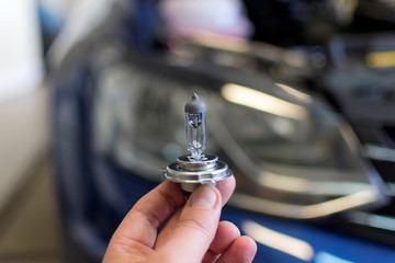 Car bulb in hand on a background of a car headlight. Car repair.