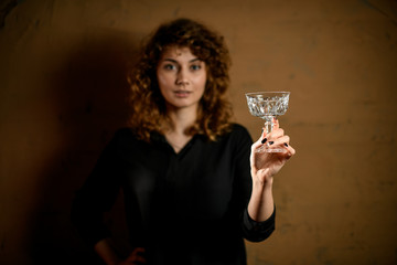 Young woman holds empty crystal glass in front of her.
