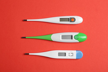 Modern digital thermometers on red background, flat lay
