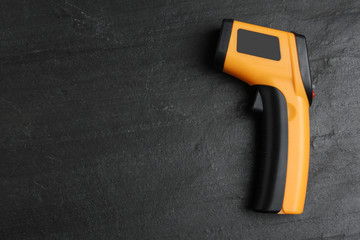 Modern non-contact infrared thermometer on black slate background, top view. Space for text