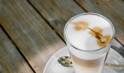Coffee cappuccino or latte in tall glass on wooden table in outdoor garden.