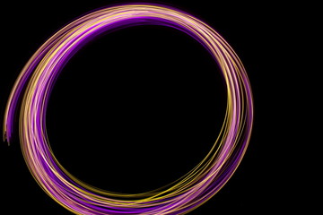Long exposure photograph of neon pink and gold colour in an abstract swirl, parallel lines pattern against a black background. Light painting photography.