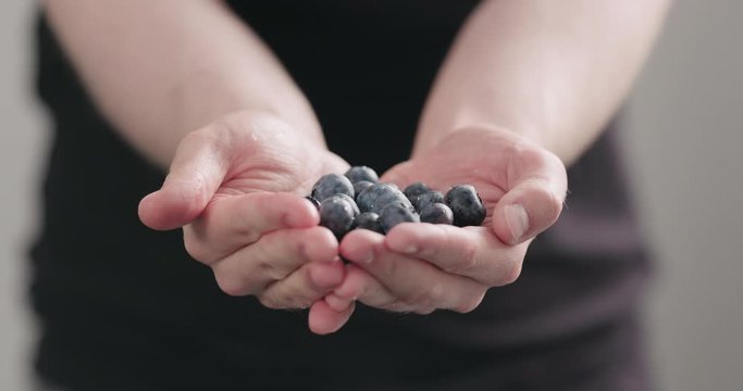 Slow motion man hands show wet washed ripe blueberries on neutral background