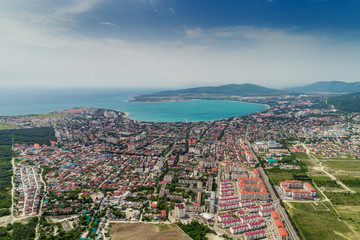 Panorama of Gelendzhik resort from a bird's-eye view. Houses and streets of the city, Gelendzhik Bay, the Caucasus mountains on the right. Sunny day, small clouds