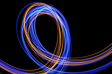 Long exposure photograph of neon blue and gold colour in an abstract swirl, parallel lines pattern against a black background. Light painting photography.