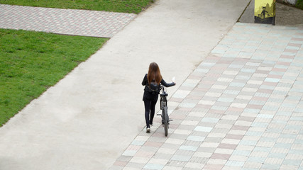 The girl goes with the bike along the path