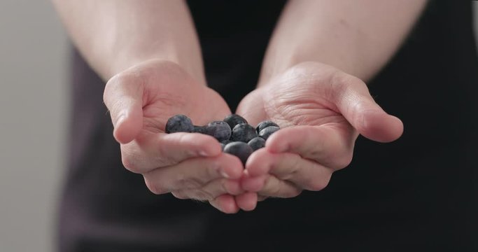 Slow motion man hands show big ripe blueberries on neutral background