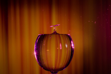 Water splash. Reaction of a falling drop on a cold water surface in a completely filled big modern glass transparent pint.Studio photo with matching orange striped colored background