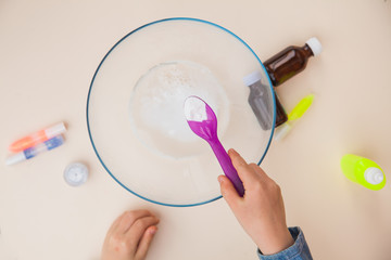 Making slime, step by step instruction, step two, adding soda. Child's hands preparing homemade toy.