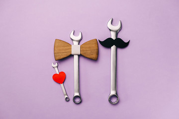 Creative flat lay composition with wooden bow tie, little heart, stylish black paper photo booth props moustaches and combination wrenches on violet background. Fathers day masculinity concept blog