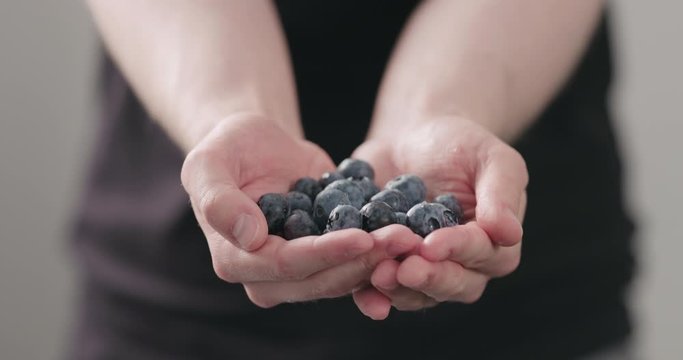 Slow motion man hands show wet washed ripe blueberries on neutral background