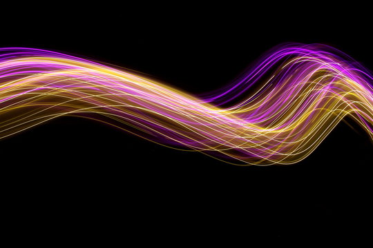 Long exposure photograph of neon pink and gold colour in an abstract swirl, parallel lines pattern against a black background. Light painting photography.