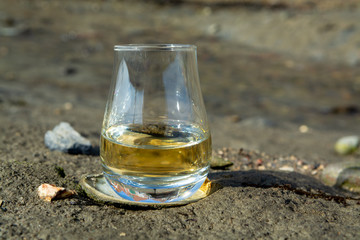 Tasting glass of Scotch whisky and sea shore during low tide, smoky whisky pairing with oysters