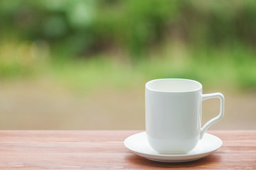 White porcelain cup on wooden table, blurred nature background