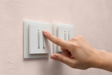 Woman pressing button of light switch indoors, closeup