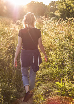 Young beautiful woman walking in field at sunset from behind 