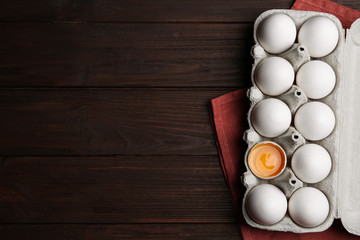 Fresh raw chicken eggs in box on wooden table, flat lay. Space for text