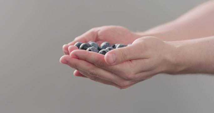 Slow motion man hands show wet washed ripe blueberries on neutral background
