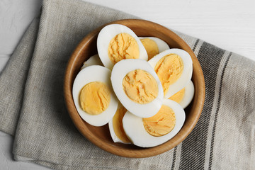 Cut hard boiled chicken eggs in bowl on table, flat lay