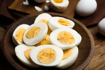 Cut hard boiled chicken eggs in wooden bowl on table