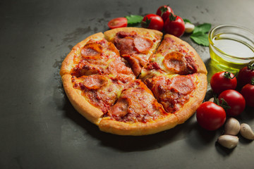 Top view of hot pepperoni pizza,Tasty pepperoni pizza and cooking ingredients tomatoes basil on black background.