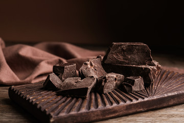 Pieces of tasty dark chocolate on wooden board