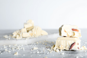 Pieces of tasty white chocolate with nuts on marble table, closeup. Space for text