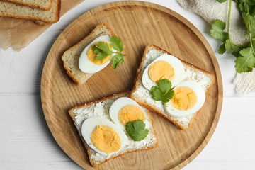 Tasty sandwiches with boiled eggs served on white wooden table, flat lay