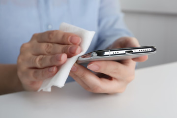 Woman cleaning smartphone with antiseptic wipe at white table, closeup