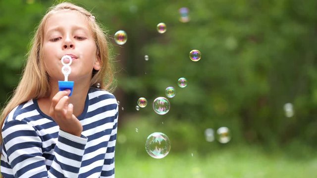 Nine-year-old girl plays with soap bubbles in the summer garden.