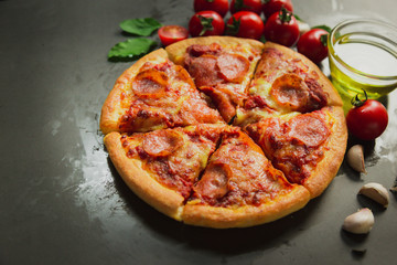 Top view of hot pepperoni pizza,Tasty pepperoni pizza and cooking ingredients tomatoes basil on black background.