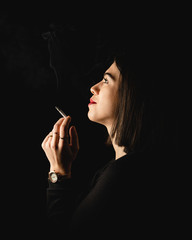 Obraz premium Low key close-up young woman smoking cigarette on black background. 