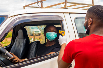 young black man wearing a nose mask, checking the temperature of a black woman driving a car