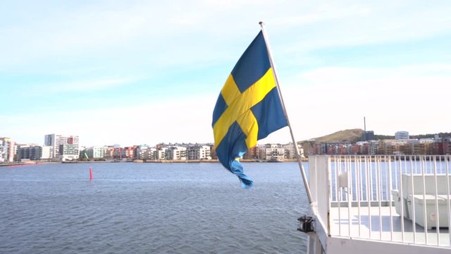 Sweden national flag is waving over the boat and blue North Sea. Sun is shining in the cloudy sky. 4K