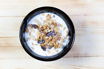Muesli with milk in black bowl on wooden table