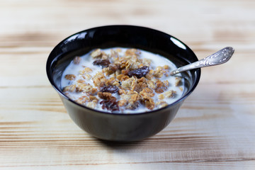 Muesli with milk in black bowl, spoon on wooden table