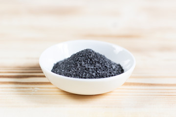 Black (burned with powder) salt in  white bowl on wooden background