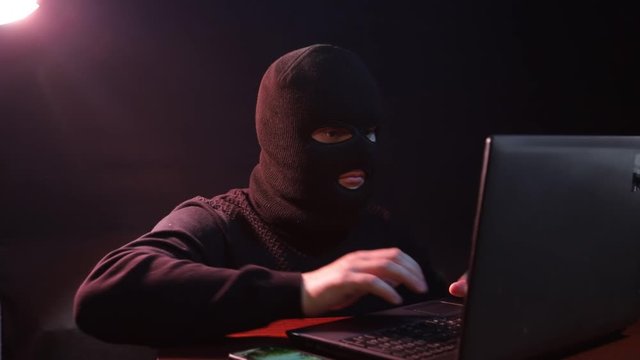 A criminal in a mask uses the Internet to steal personal data,