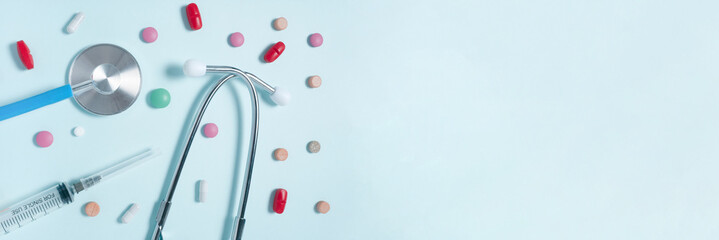 Stethoscope, different colorful pills in blisters, syringes on a light blue background. Medicine background.