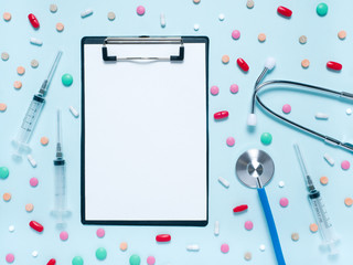 Stethoscope, different colorful pills in blisters, syringes and empty blank for prescription on a light blue background